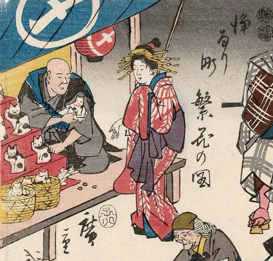 Detail from Utagawa Hiroshige‘s ukiyo-e style woodblock print from the series, “Flourishing Business in Balladtown,” showing a vendor selling maneki-neko statues to a woman
