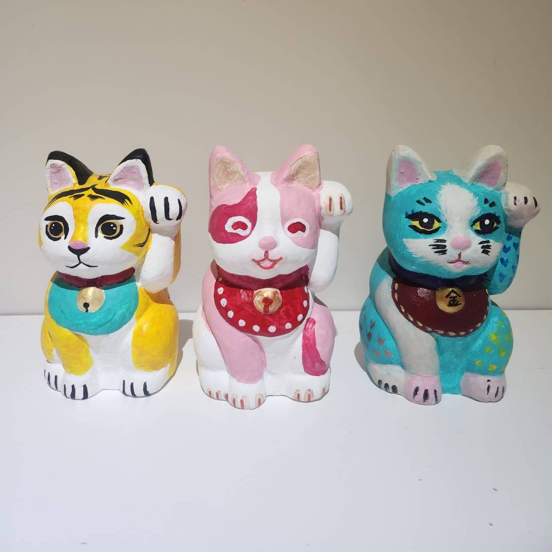 Three unique Maneki Neko figurines, each customized with different colors and patterns.